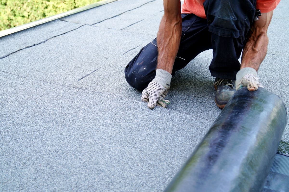flat roof replacement cost worker holding bitumen roll