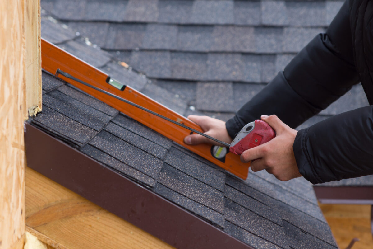how to measure roof pitch Roofer holding a tape measure and spirit level in his hands over newly installed tiles on a new build wooden house